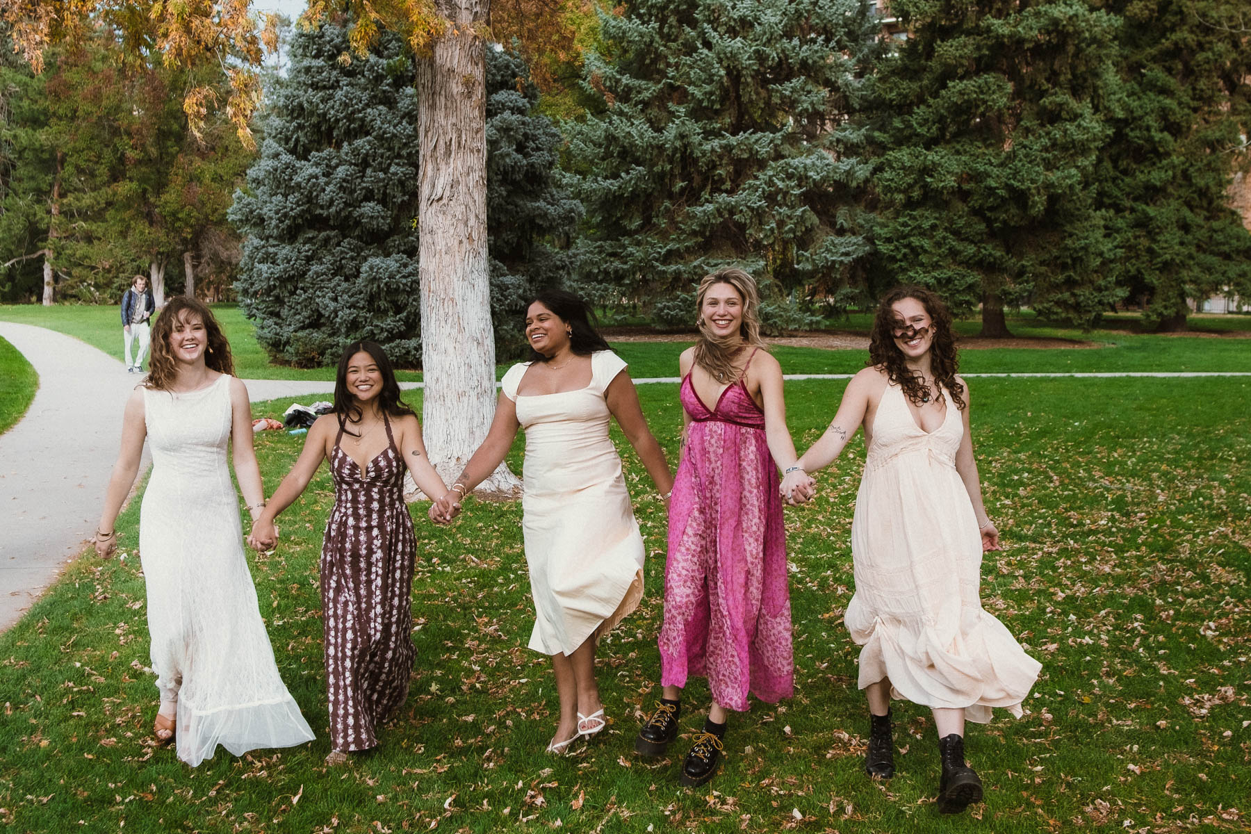 Group of friends in dresses walking hand-in-hand through a park